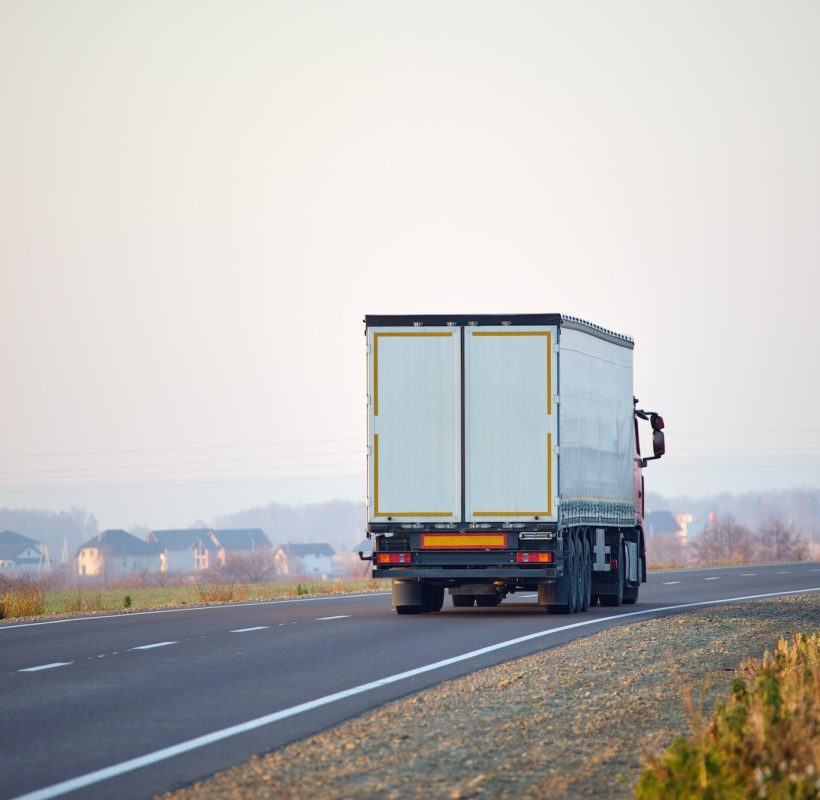 Semi-truck with cargo trailer driving on highway hauling goods in evening.